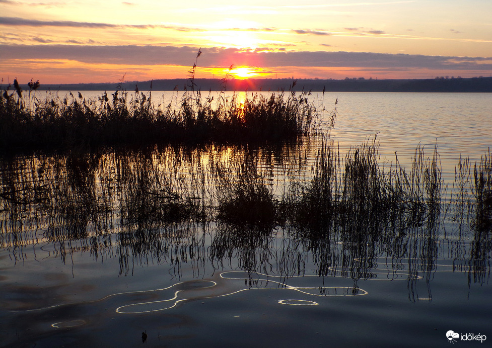 A kondenzcsík tükörképe a hullámzó tavon