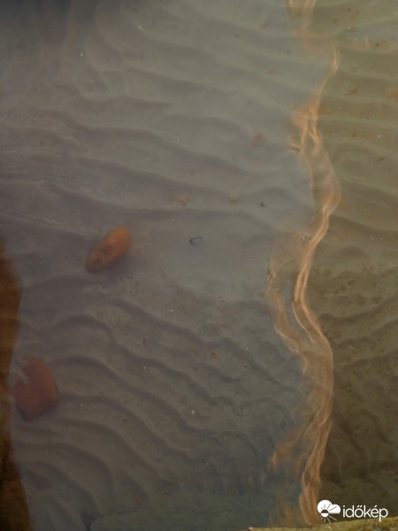 A még fel nem kavarodott iszap hullámos látványa a kövek között